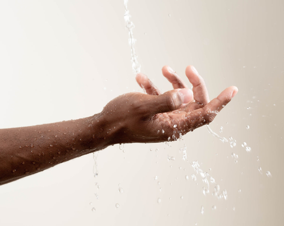 A hand touching water from a water-saving showerhead
